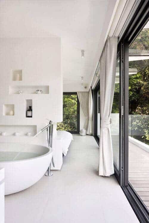 Modern spa bathroom featuring a freestanding oval bathtub, large glass windows, calming neutral colors, and stylish built-in shelves.