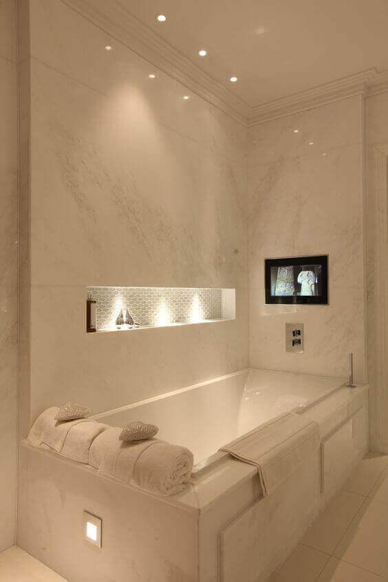 Luxury spa bathroom with large marble tiles, elegant recessed lighting, a 6x3 feet bathtub, and a flat-screen TV for a serene retreat.