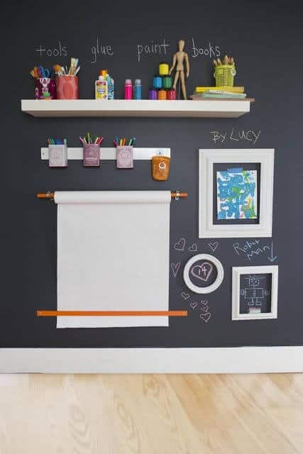 Creative wall storage in a basement playroom features a dark wall backdrop, a white shelf with art supplies, and organized containers, fostering a fun atmosphere.