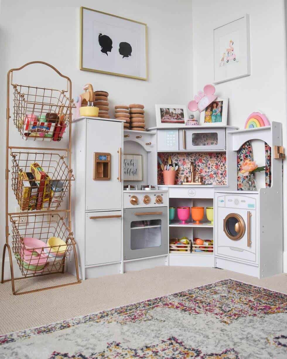 Compact play kitchen with stove, oven, and refrigerator. Features open shelving, colorful play food, and a soft rug for comfort.