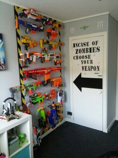 Toy gun display wall with vibrant Nerf blasters in a playful basement playroom. Whimsical sign reads, "Incase of Zombies Choose Your Weapon."