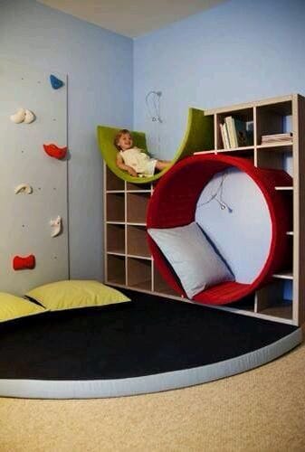 Kids playroom with a climbing wall, padded play area, green cushions, built-in shelving for toys, and vibrant light blue walls.
