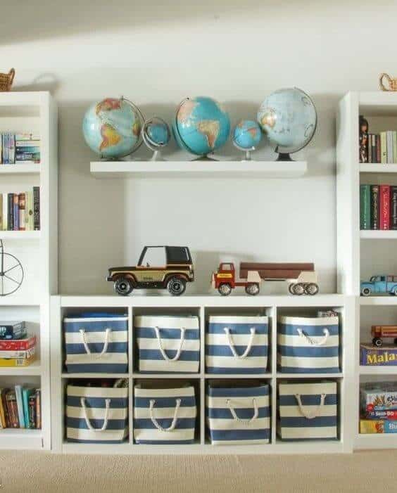 Children's bookshelf with open shelving, white wood, five decorative globes, two vintage toy vehicles, and nine blue-striped fabric bins.