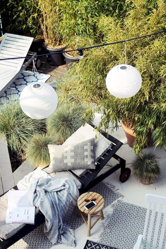 Cozy outdoor relaxation area with a minimalist chaise lounge, paper lanterns, and lush potted plants, ideal for budget-friendly backyard makeovers.