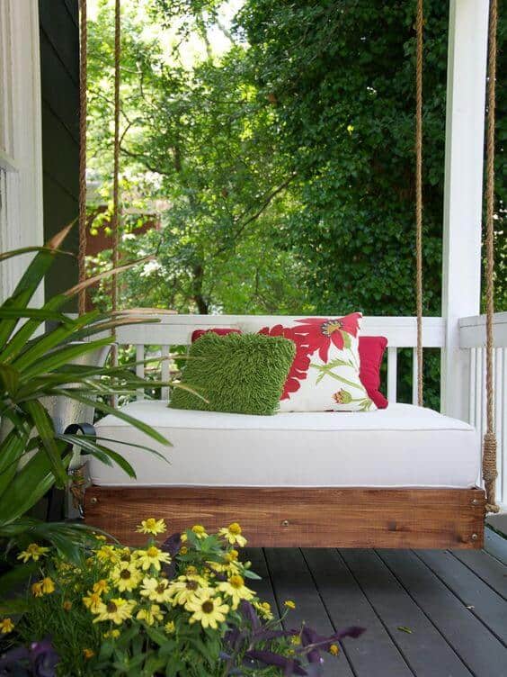 Suspended swing bed made from sturdy wood, adorned with vibrant cushions, surrounded by lush greenery and colorful flowers, perfect for a cozy backyard oasis.