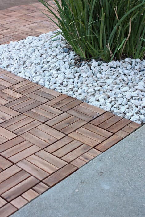 Intricate herringbone-patterned wooden deck with warm tones, bordered by low-maintenance grasses, enhancing outdoor living space aesthetics.