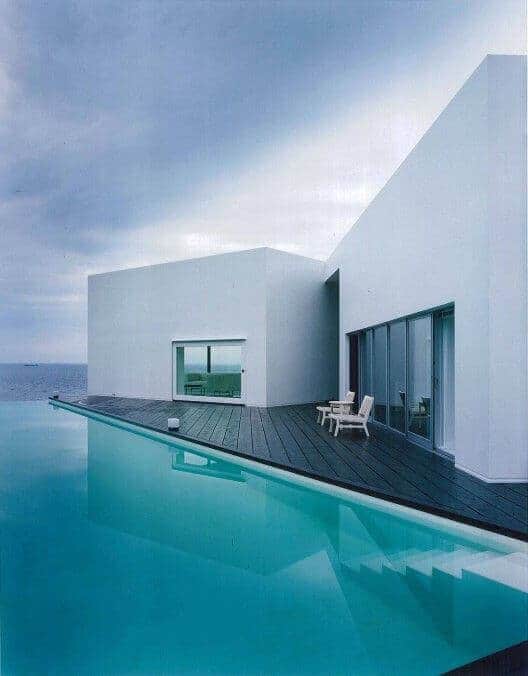 Contemporary deck design with smooth white walls and large glass panels, featuring a cantilevered deck over an infinity pool.