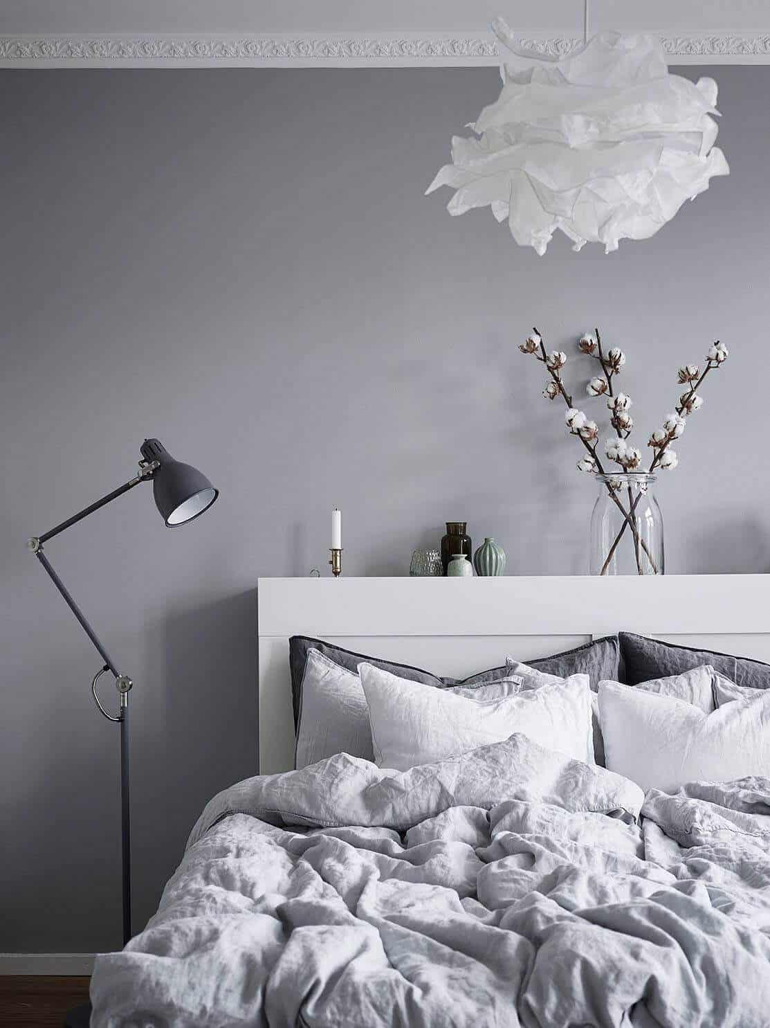 Minimalist gray bedroom showcasing soft textures and muted colors. Light gray walls, plush bedding, and a sculptural pendant light create a serene atmosphere.