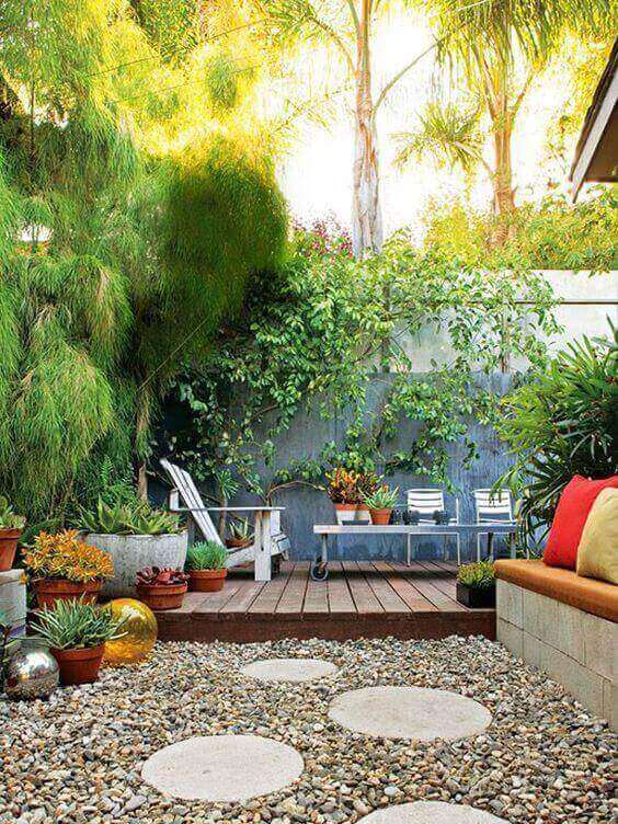 Cozy small backyard deck with a gravel pathway, circular stepping stones, and a wooden bench, surrounded by lush greenery and succulents.
