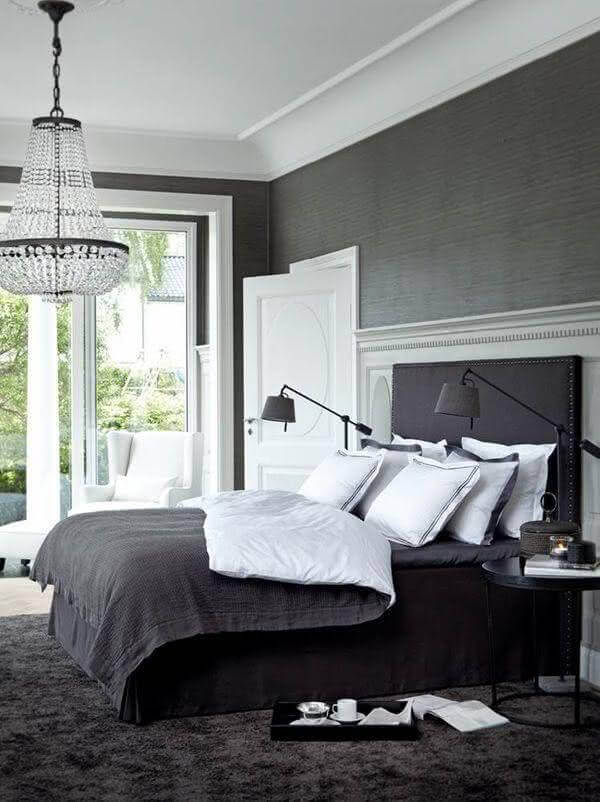 Modern grey bedroom with dark gray walls, a plush black bed, and white linens. Features a stylish chandelier and large glass doors to a garden view.