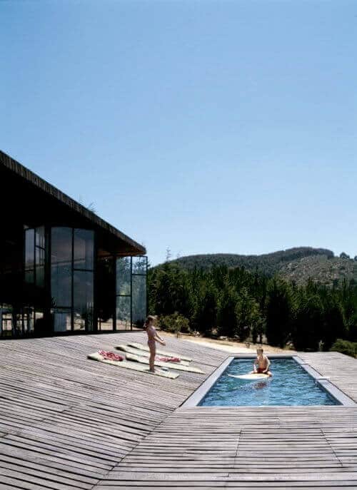 Sleek wooden deck surrounding a rectangular swimming pool, with colorful sun loungers and lush greenery, creating a luxurious outdoor living space.