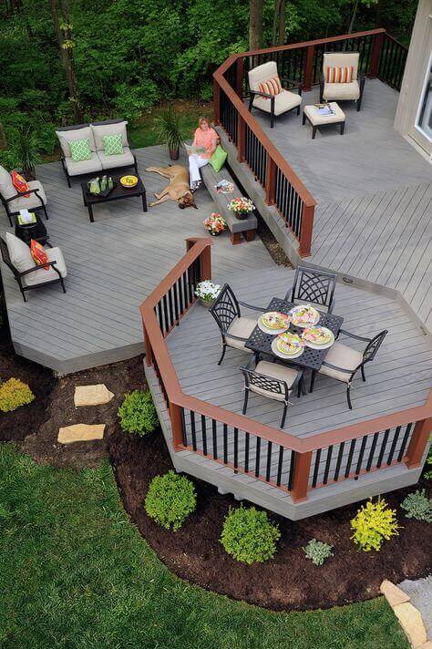 Multi-level deck features a dining area with a hexagonal table and cushioned sofas, surrounded by vibrant landscaping, ideal for outdoor living.