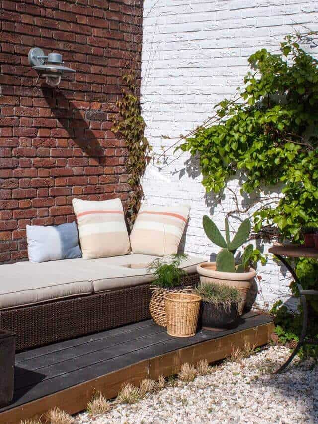 Plush, light-colored sectional sofa with striped cushions on a wooden deck, surrounded by potted plants and a stylish light fixture.