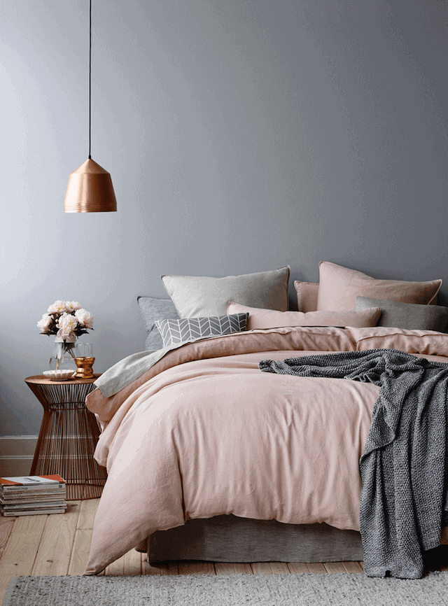 Cozy grey bedroom with a low-profile bed against a smooth gray wall, soft pink duvet, plush pillows, and a warm wood floor.