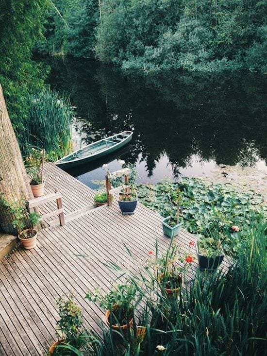 Wooden dock leading to serene waters, flanked by potted plants and a green rowboat, perfect for outdoor living and gatherings.