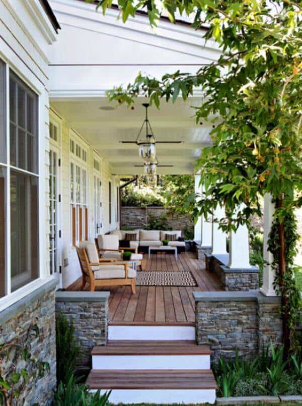 Spacious porch with a composite wood deck, stone pillars, and cozy seating, perfect for outdoor living in temperate climates.
