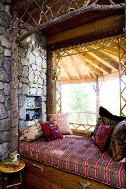 Cozy window seat with a multi-colored striped cushion, wooden base, and natural stone walls, perfect for a reading nook.