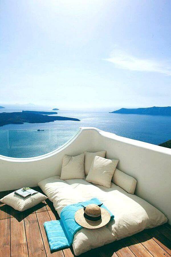 Tranquil reading nook with a plush mattress, cream cushions, and a turquoise throw, framed by white walls and wooden decking, perfect for relaxation.