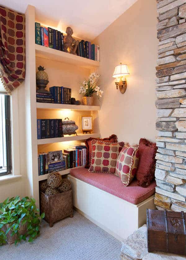 Cozy reading nook with plush cushions, custom shelving, decorative pillows, and warm LED lighting. Features a stone fireplace and natural light.