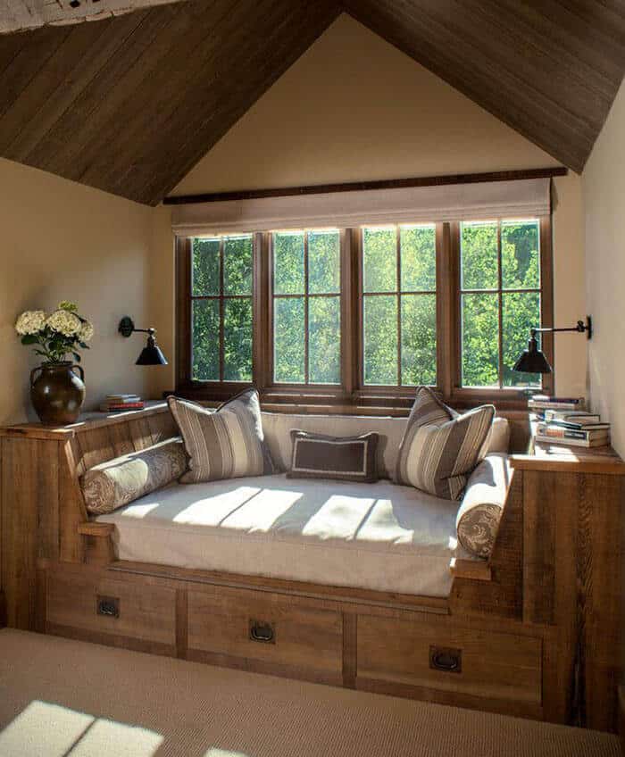 Cozy reading nook featuring a wooden bench with plush cushions, large windows, and a stylish lamp, perfect for a serene retreat.