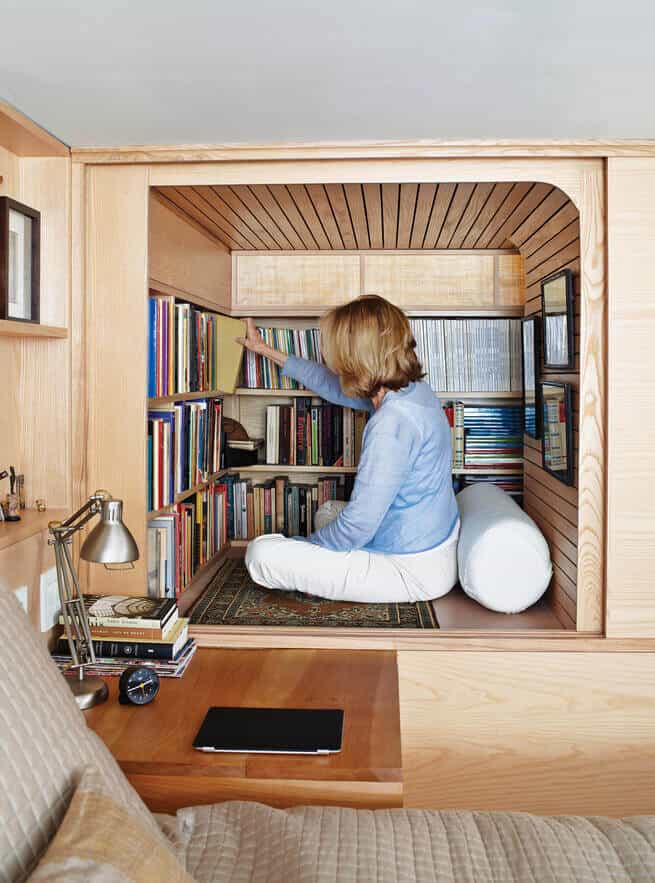 Cozy reading nook with natural wood finishes, built-in shelves, cushioned seating, and a small desk with a lamp, perfect for study or relaxation.
