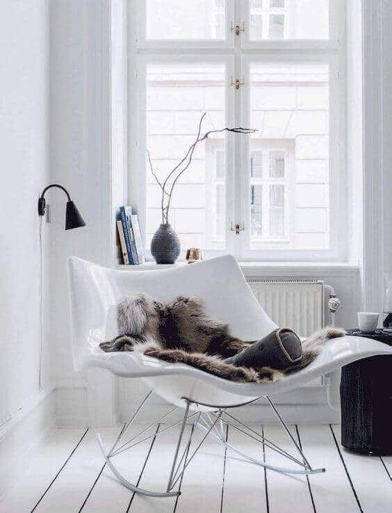 Cozy reading nook with a modern lounge chair, soft fur throw, small black side table, and a contemporary floor lamp. Natural light floods the bright room.