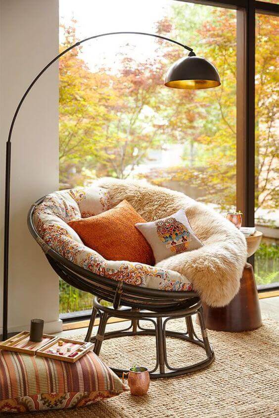 Cozy reading nook with a modern round chair, floral upholstery, and soft pillows. Natural light and autumn views create a warm ambiance.