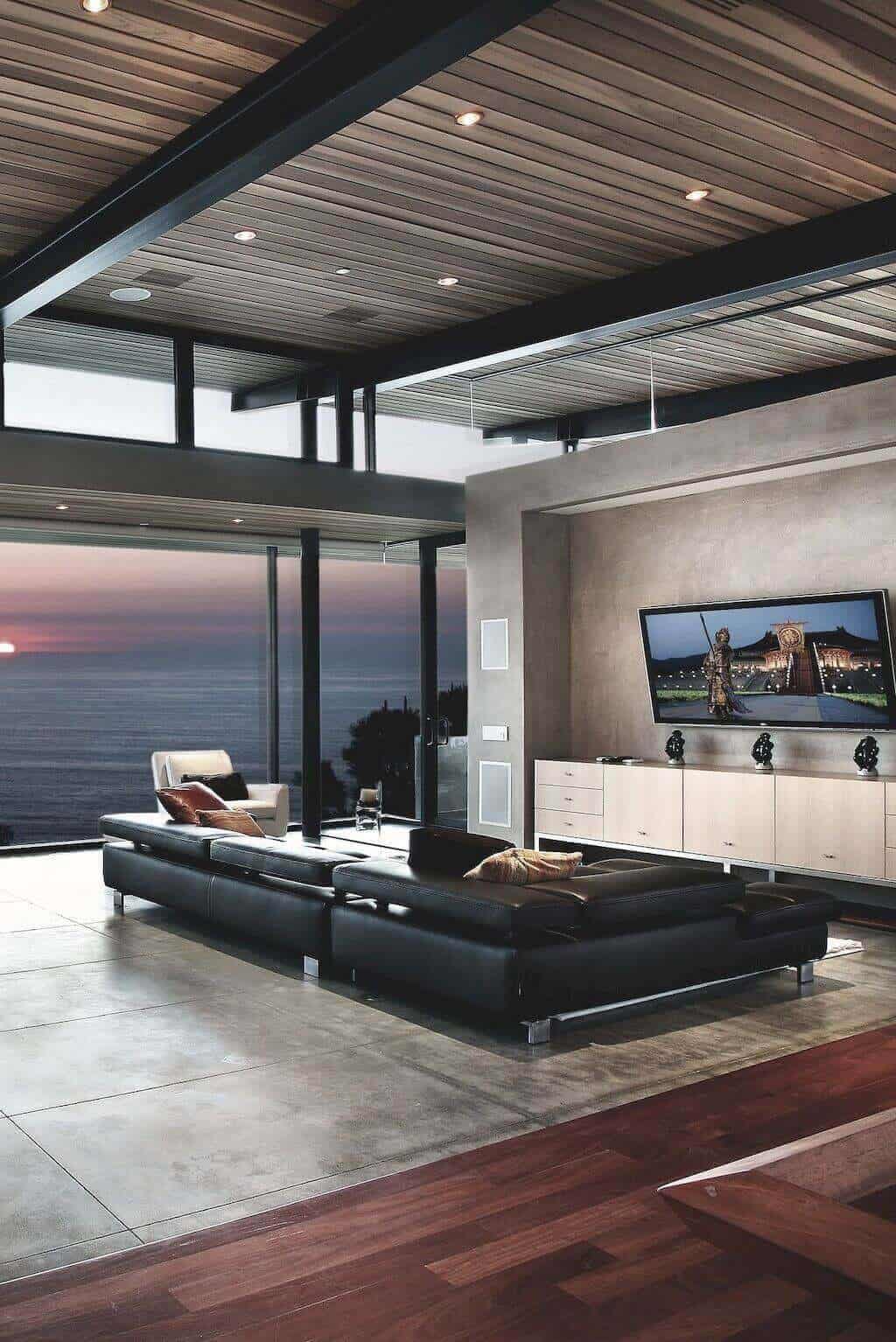 27 Contemporary Living Room Ideas for a Modern Haven Space 16 Contemporary living room with floor-to-ceiling windows, black leather sectional, wooden armchair, and polished concrete flooring.