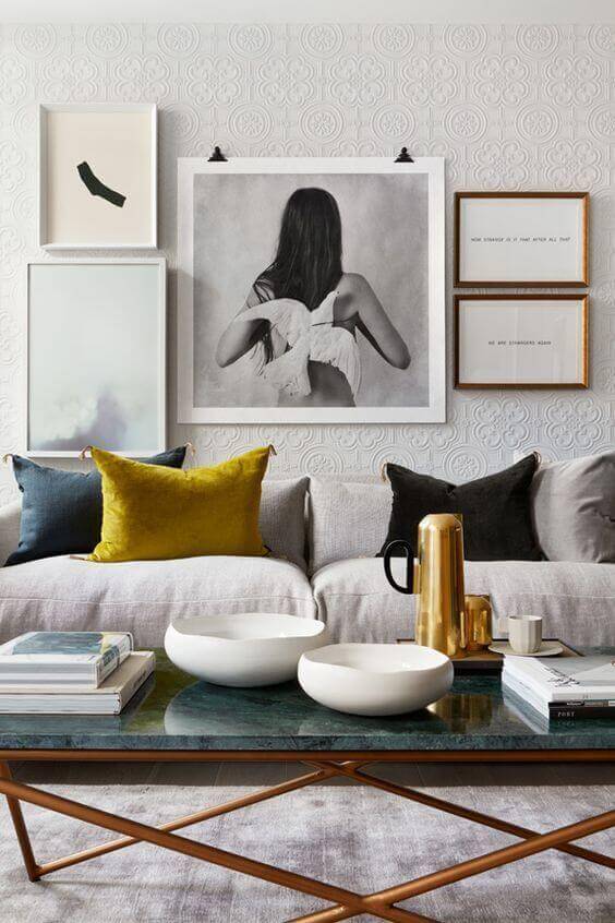 27 Contemporary Living Room Ideas for a Modern Haven Space 21 Modern living room with a neutral palette; gray sofa, mustard and navy pillows, glass coffee table, textured wallpaper, and art prints.