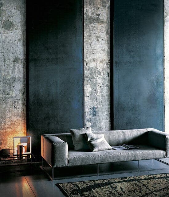 27 Contemporary Living Room Ideas for a Modern Haven Space 5 Sleek gray sofa against textured concrete walls, flanked by dark panels. A warm lamp on a minimalist table, with a vintage-style rug beneath.