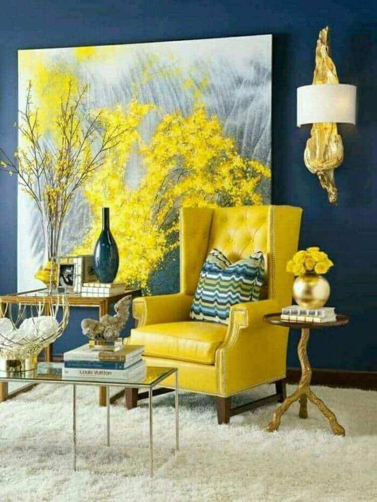 27 Contemporary Living Room Ideas for a Modern Haven Space 9 Vibrant yellow wingback chair against a navy blue wall, with an abstract painting, glass coffee table, and yellow floral decor.
