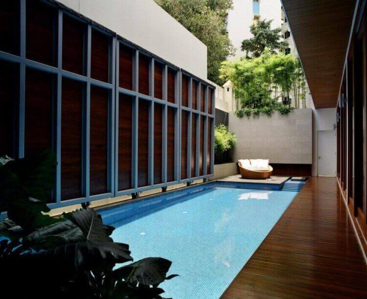 Sleek indoor swimming pool design featuring turquoise mosaic tiles, surrounded by wooden panels and lush greenery, with a lounge chair for relaxation.