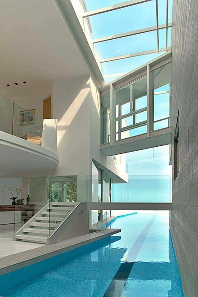 Spacious modern indoor pool area featuring glass walls, polished stone, and a minimalist staircase, emphasizing natural light and open design.