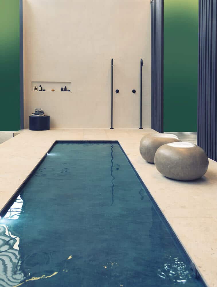 Serene indoor swimming pool design featuring light-colored stone flooring, minimalistic elements, and natural daylight, enhancing tranquility.