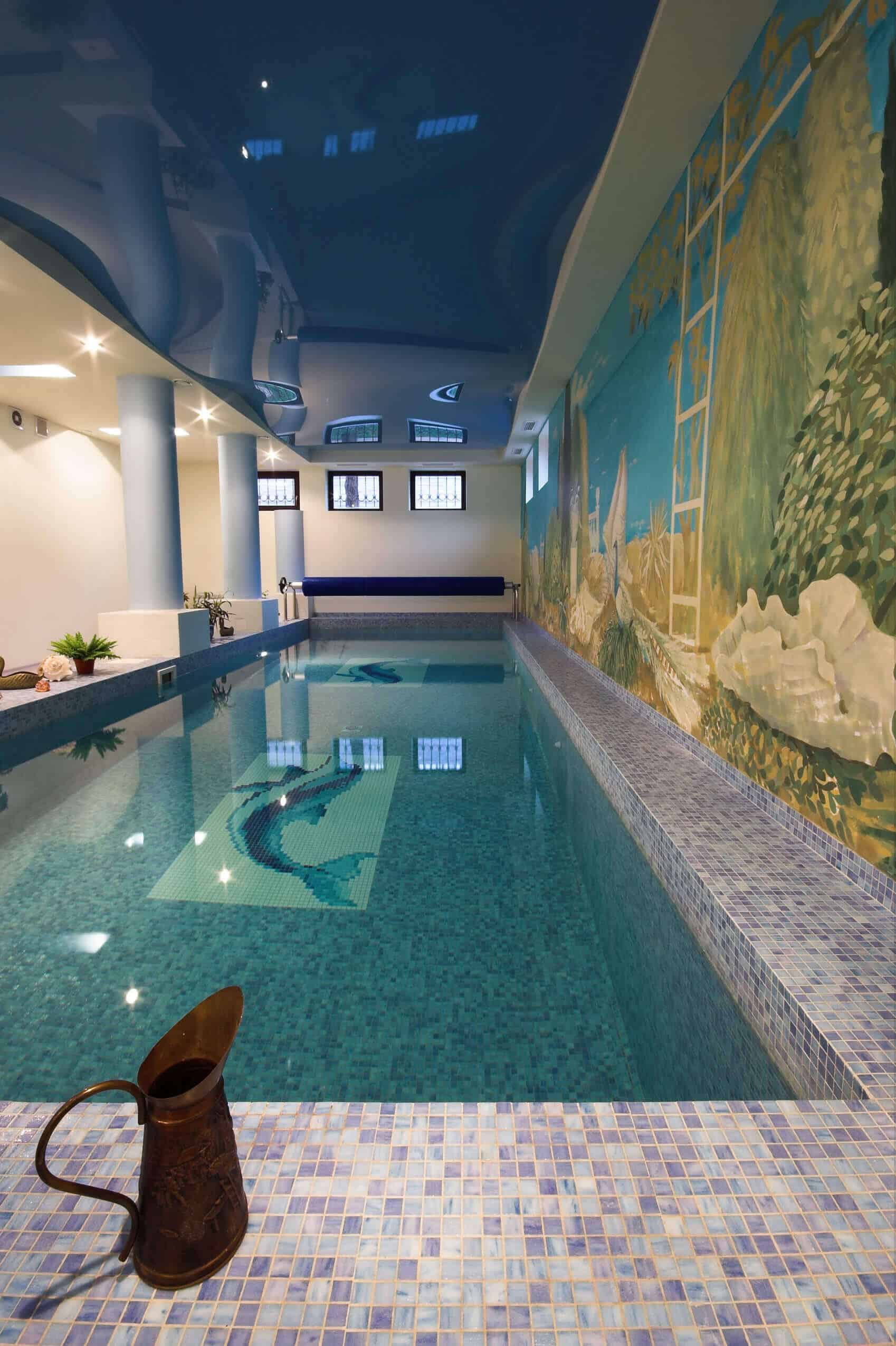 Indoor swimming pool with mosaic tile bottom featuring a dolphin design. Bright area with recessed lighting and a serene underwater mural.