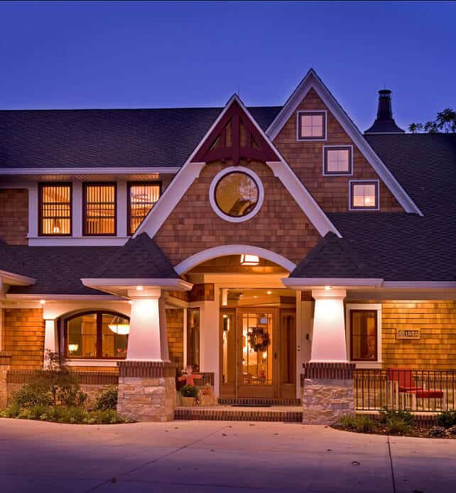 Craftsman-style home featuring a grand entry with large arched and circular windows, complemented by stone accents and a welcoming porch.