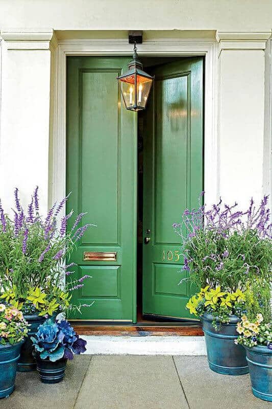 Vibrant green front door flanked by dark teal pots with yellow flowers and purple lavender, featuring a classic lantern above.