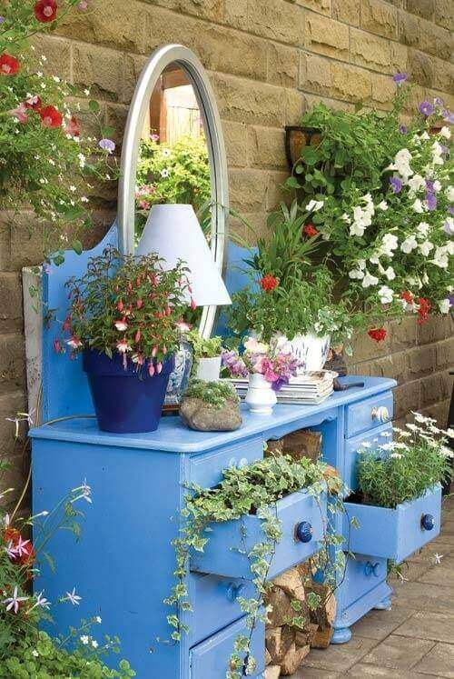 Vibrant blue garden furniture provides storage and displays plants, surrounded by potted flowers and cascading vines against rustic stone walls.