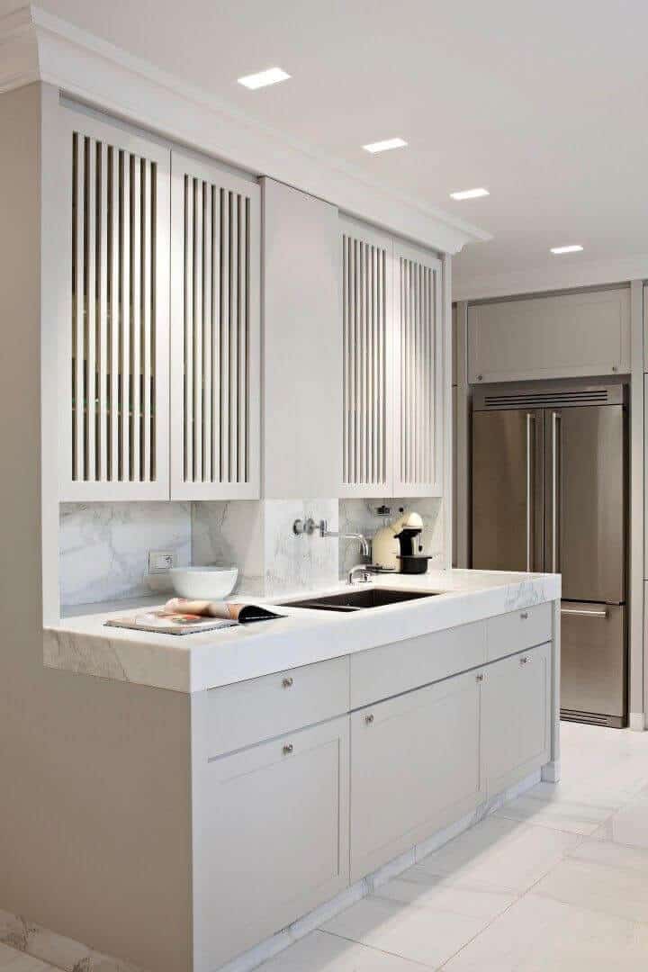 Sleek kitchen with white cabinetry and marble countertops. Features vertical slat upper cabinets, deep integrated sink, and brushed nickel fixtures.