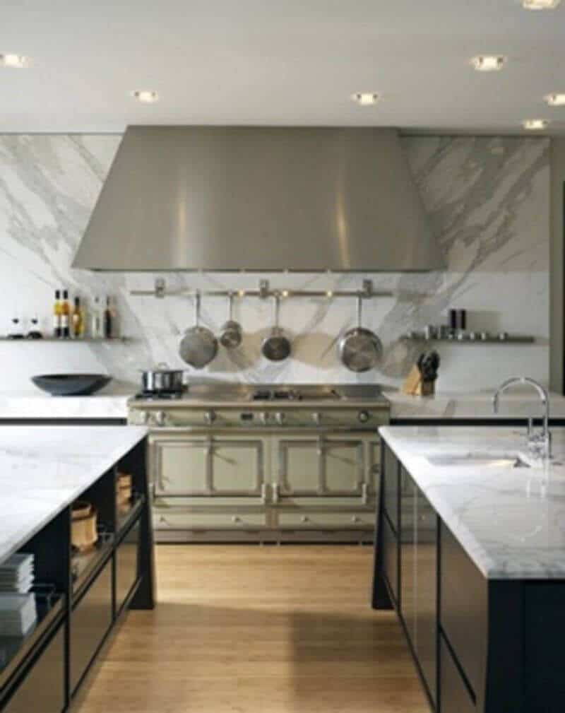 Modern kitchen with two large islands featuring white marble countertops, matte black cabinetry, and a professional-grade stove, all illuminated warmly.