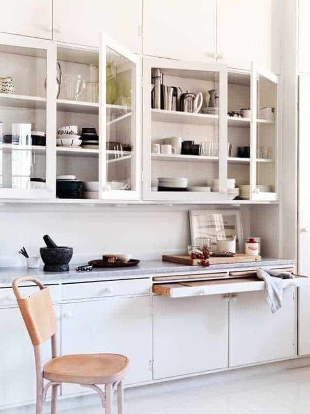 Minimalist kitchen with white cabinets showcasing dishware, smooth countertop, and a wooden drawer for organized storage solutions.