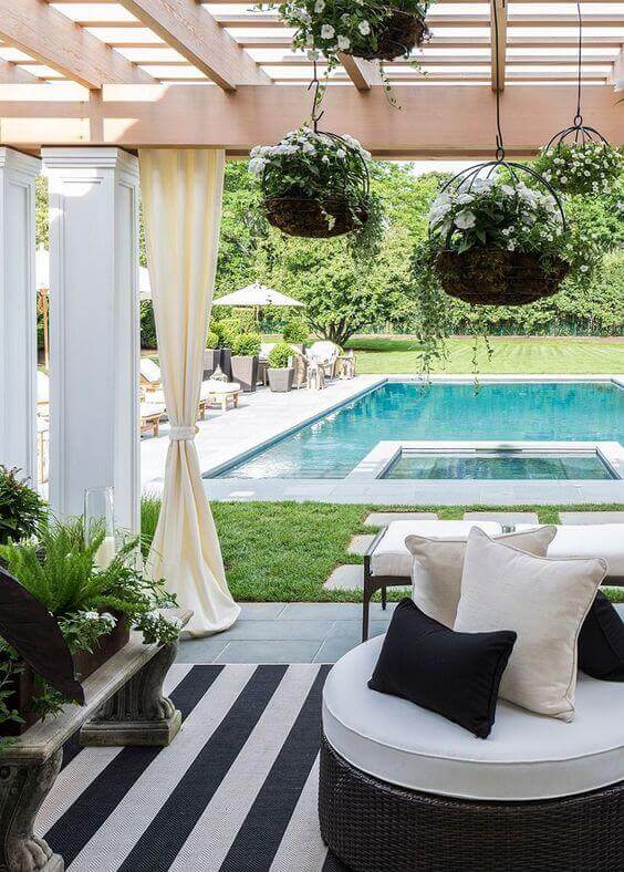 25 Pool Pergola Ideas for a Relaxing Oasis 19 Outdoor space with a round sectional sofa, a pergola providing shade, and a rectangular pool with an attached spa, featuring lush greenery.