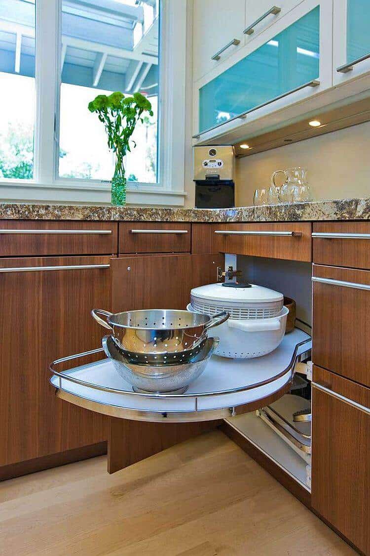 Modern pull-out shelf in a kitchen, crafted from polished wood, optimizing corner space for a colander and large bowl. Bright, airy atmosphere with granite countertops.