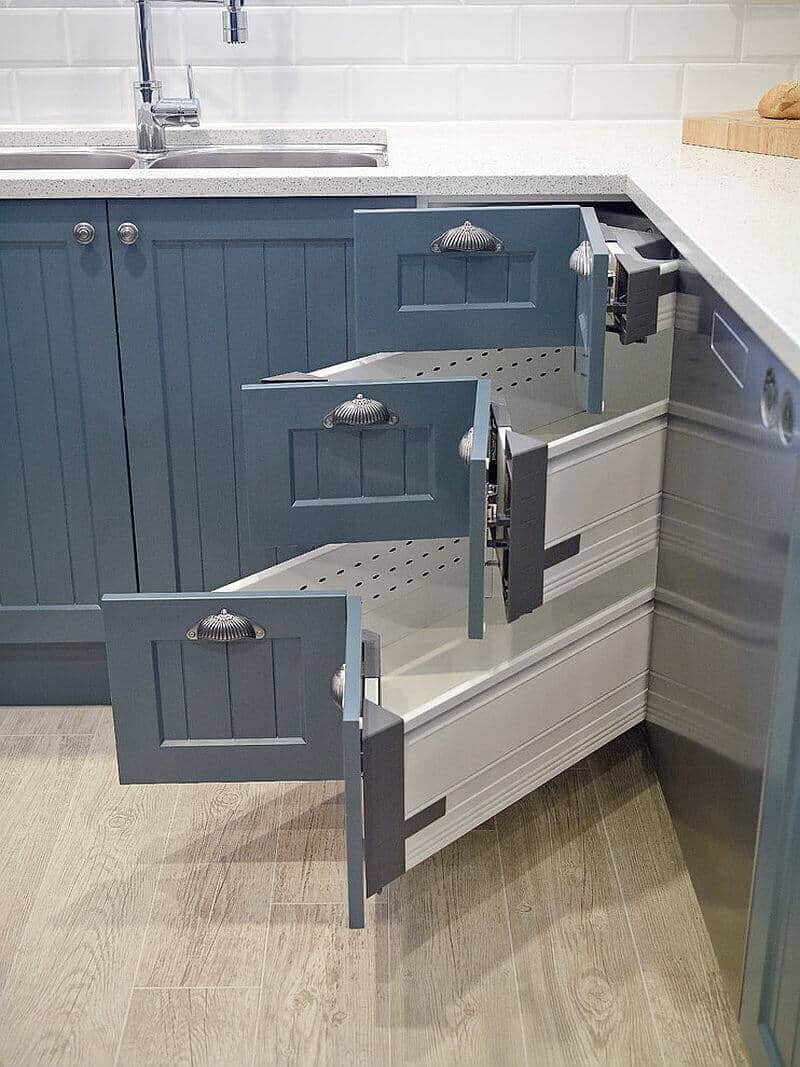 Deep blue cabinetry features pull-out drawers for easy access, enhancing kitchen organization. Metallic handles contrast with wood finishes, creating a modern, functional space.