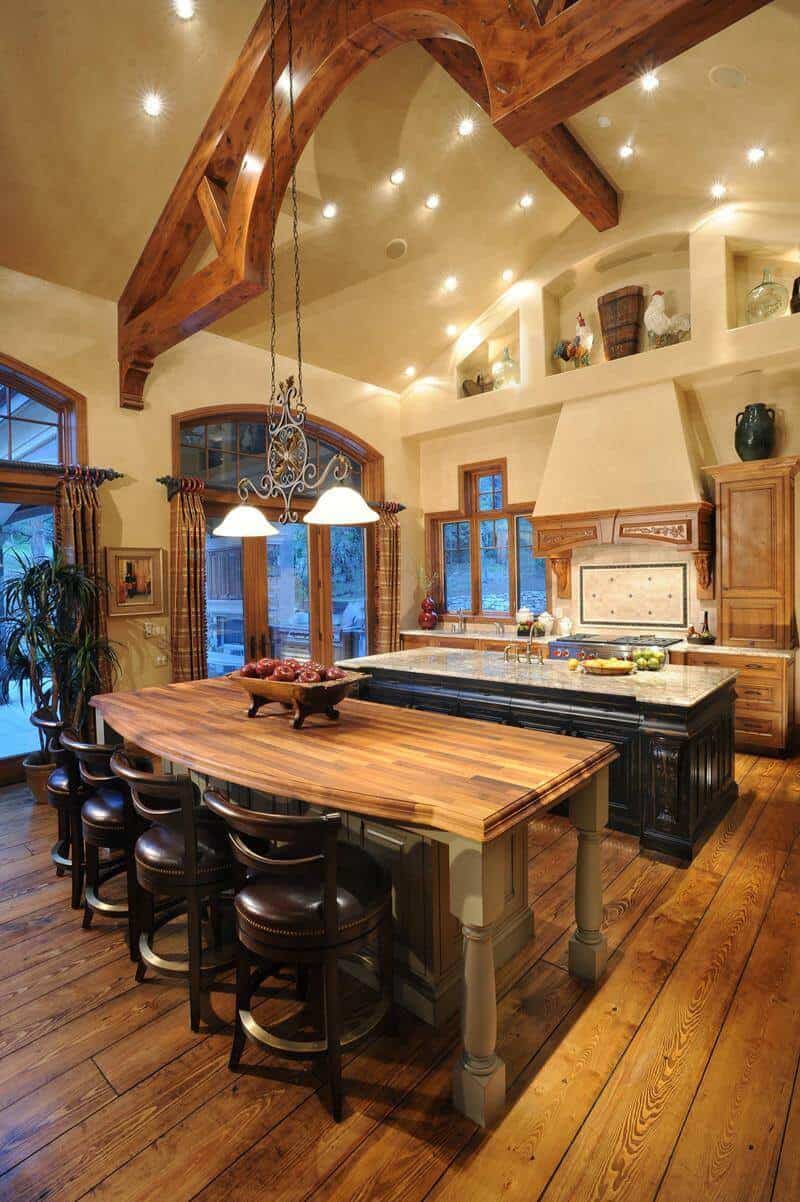 Spacious kitchen with double islands, vaulted ceilings, dark wooden flooring, and natural light from large windows.
