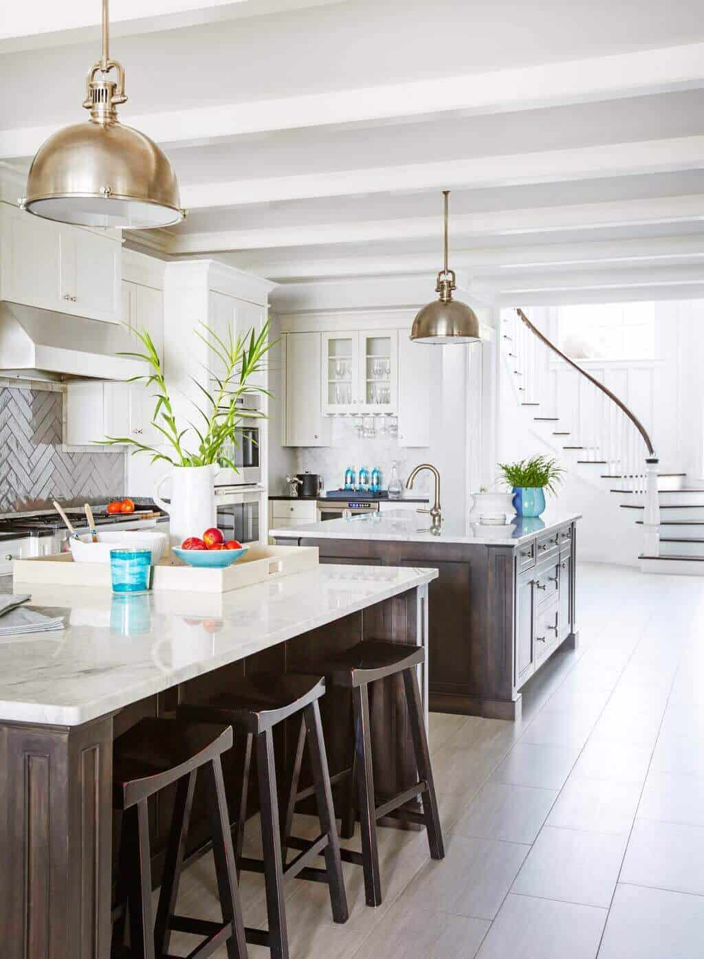 Large double island kitchen features marble countertops, white cabinetry, and brushed brass pendant lights, enhancing functionality and style.