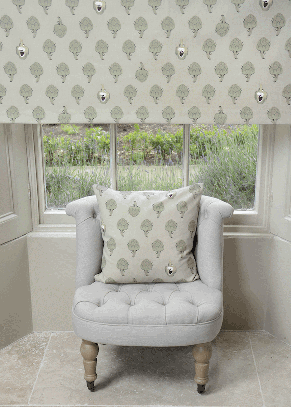 Cozy bedroom featuring sage green decor with a tufted chair, botanical cushion, and natural light enhancing the inviting atmosphere.