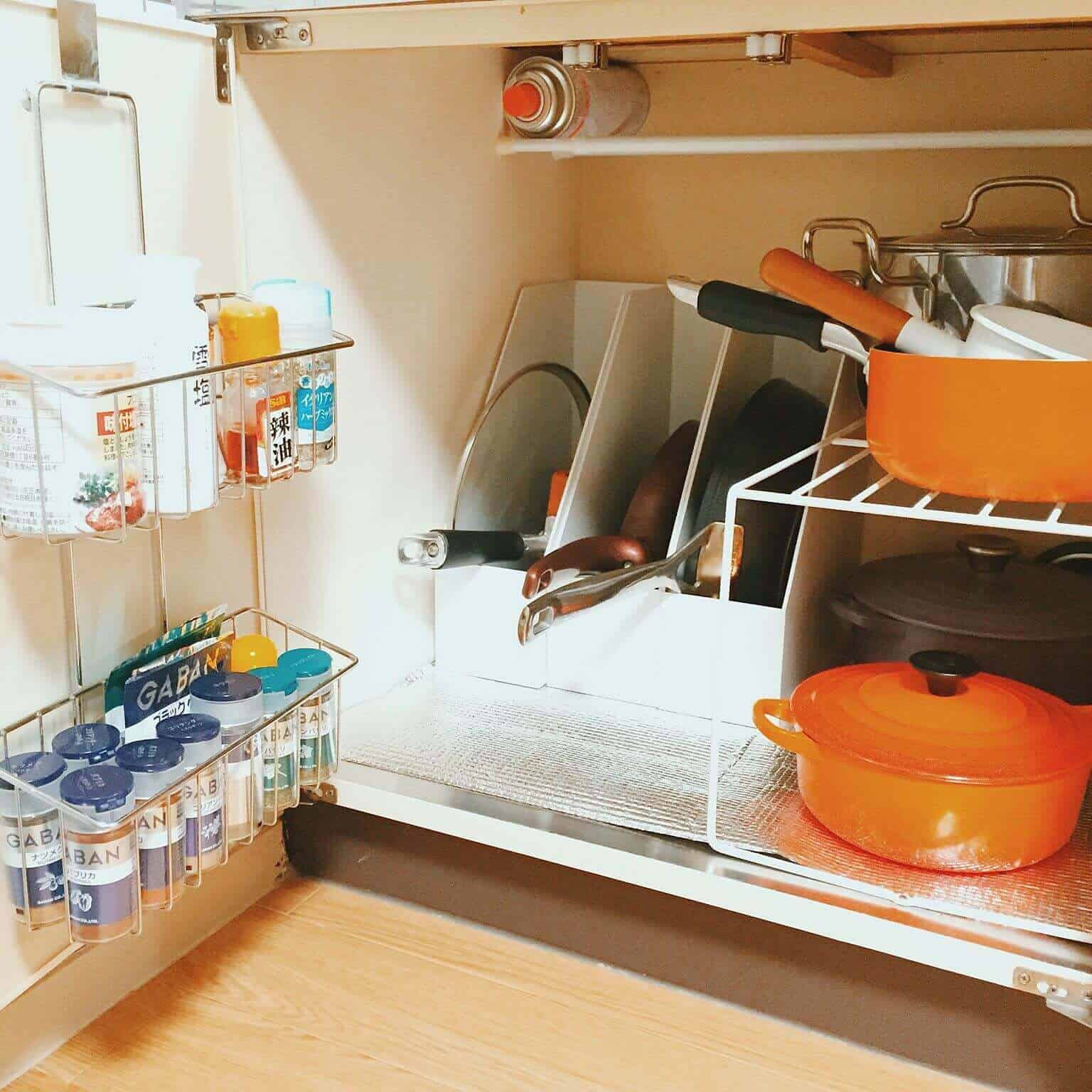 Organized kitchen cabinet featuring wire racks and a horizontal shelf, efficiently storing cookware and spice jars in a light wood finish.