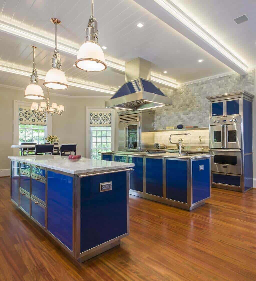 Spacious modern kitchen with two islands featuring white marble countertops, blue cabinetry, stainless steel appliances, and hardwood flooring.