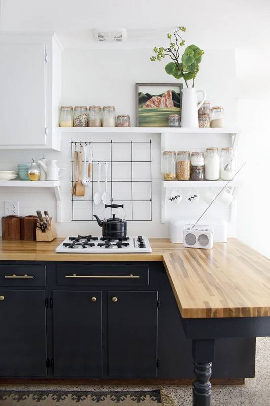Modern kitchen featuring black cabinetry, wooden countertop, open shelving with glass jars, and wall-mounted utensil grid for clever organization.